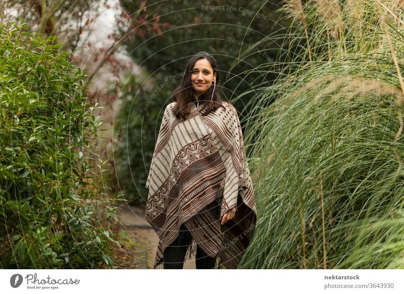 Junge Frau mit Poncho, die im Herbst zwischen hohem Gras posiert. Ethnie der Indianer nahöstliche Ethnie Kopfhörer mittlere Aufnahme Hörbuch