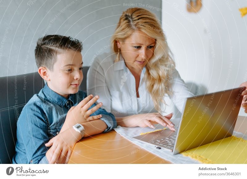 Positive Mutter mit Sohn am Laptop modern heimwärts Schulbildung Inhalt Browsen benutzend Wohnzimmer Eltern Tutorin lernen Lehrer Lektion Tisch Netbook