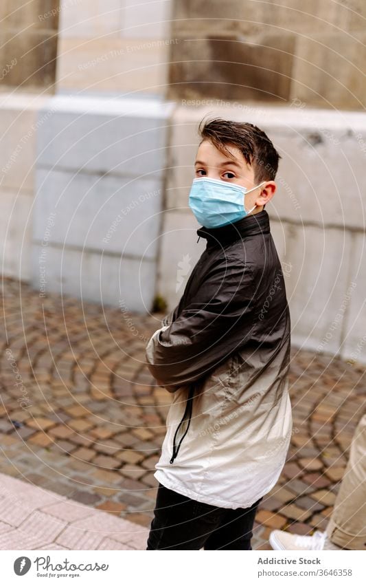 Junge mit Schutzmaske geht auf der Straße Mundschutz Atemschutzgerät Bürgersteig Spaziergang ernst lässig schlendern Coronavirus Seuche Jacke verschränkte Arme