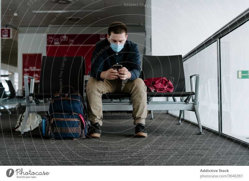 Männlicher Passagier in Atemschutzgerät mit Smartphone beim Warten auf den Flug Mann Browsen Mundschutz Flughafen Coronavirus Gerät warten reisen Seuche