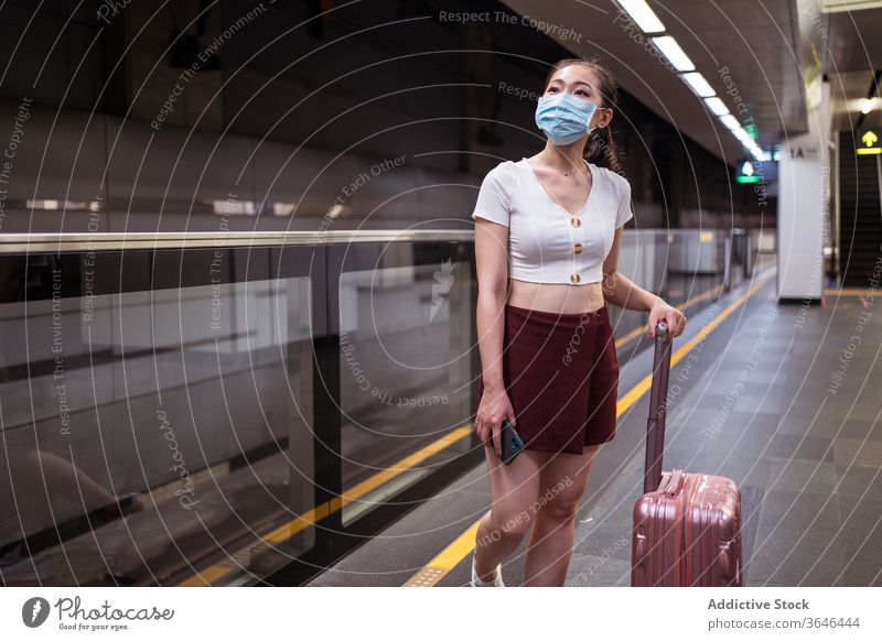 Stilvolle Asiatin mit Atemschutzmaske und Koffer wartet auf den Zug Frau Bahnhof Spaziergang reisen Atemschutzgerät stehen Podest Coronavirus Passagier Bund 19