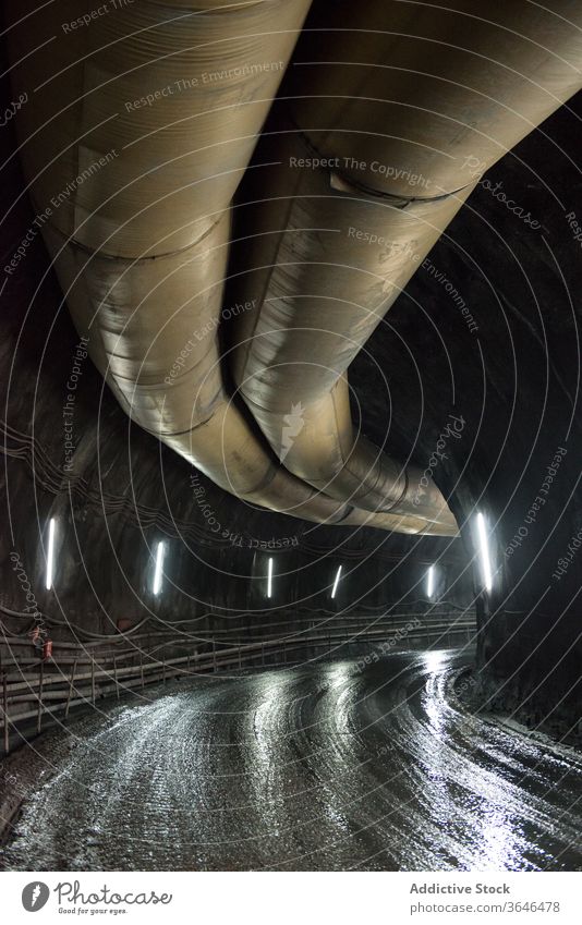 Unterirdisch beleuchteter Tunnel mit Pipeline Bergbau Stollen Durchgang Röhren Metall Licht leuchten unterirdisch Konstruktion Struktur Stein riesig breit