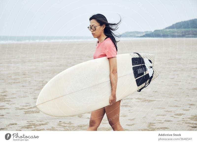 Zufriedene Surferin, die mit einem Surfbrett am Strand spazieren geht Frau Spaziergang sandig führen Inhalt MEER lässig Seeküste sorgenfrei Aktivität jung