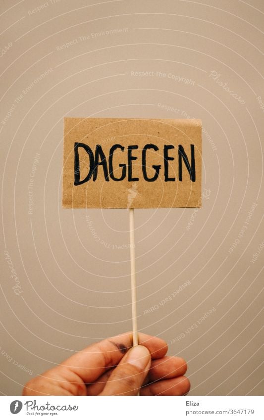 Eine Hand hält ein Schild mit der Aufschrift DAGEGEN. Protest. Demonstration. Anti. dagegen ablehnend protestieren demonstrieren Dagegen sein Nein Weigerung