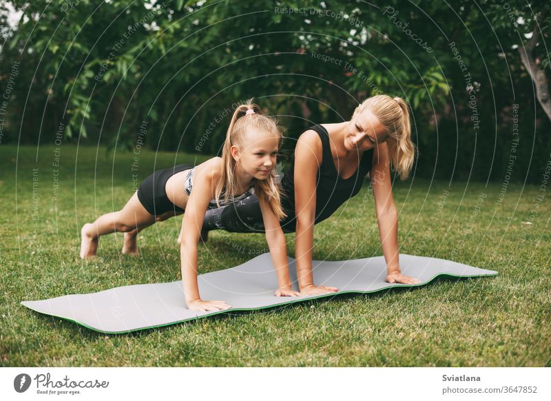 Mutter und Tochter treiben auf dem grünen Rasen in der Nähe ihres Zuhauses Sport. Sport und Fitness im Freien. Gesunde sportliche Lebensweise Yoga Lifestyle