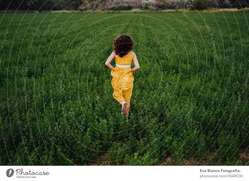 Porträt einer jungen schönen Frau, die ein gelbes Kleid trägt und in einem grünen Feld läuft. Sommerzeit und Lebensstil 1 Schönheit sorgenfrei lässig Kaukasier