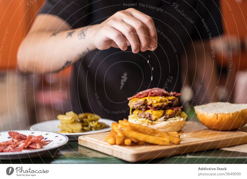 Männlicher Koch bestreut Burger mit Salz hinzufügen Mann vorbereiten geschmackvoll lecker Kotelett Café männlich Tisch Küchenchef Mittagessen Mahlzeit