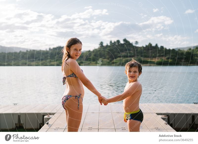 Geschwister auf Holzsteg, die Hände halten Pier See Kinder Sommer Urlaub Geschwisterkind Zusammensein Badebekleidung Kai Bruder Schwester Einheit