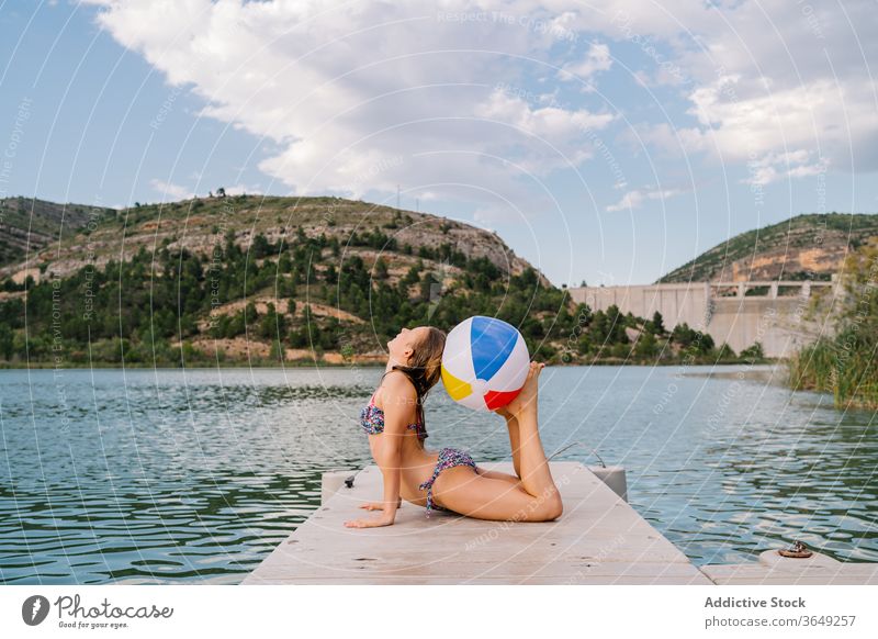 Teenager-Mädchen macht Yoga in King-Cobra-Pose am Pier Königskobra-Pose beweglich üben See Sommer raja bhujangasana Beachball Badebekleidung Übung Gesundheit