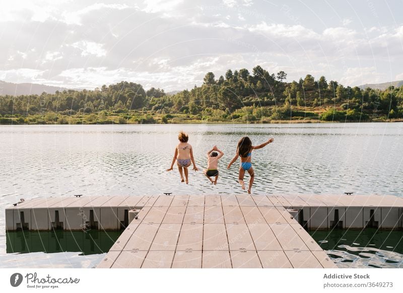 Begeisterte Geschwister springen vom Pier in den See Kinder Spaß haben Wasser Menschengruppe Geschwisterkind Moment Teich Kindheit Badebekleidung Kai hölzern