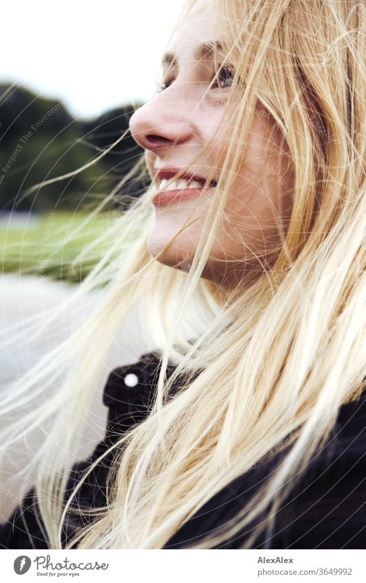 Seitliches Portrait einer jungen, blonden, lächelnden Frau junge Frau schön schlank seitlich langhaarig windig ästhetisch Sommer Ausflug Schönes Wetter Model