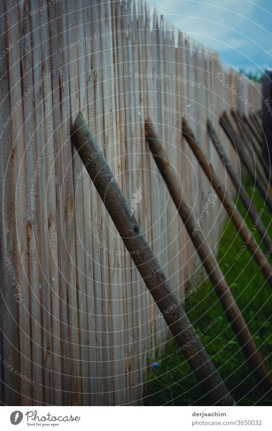 Intelligente Lösung - einfach  gut und   billig. Holzstangen stehen als Stütze an einem Bretterzaun. bretterwand Außenaufnahme Farbfoto Menschenleer Natur Tag