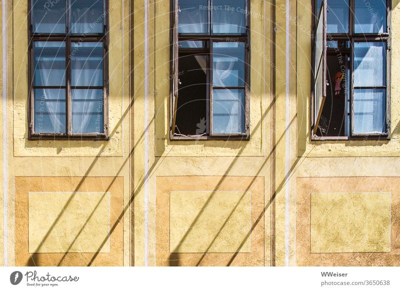 Schräge Schatten auf einer alten Fassade Fenster offen Diagonale Gardinen Vorhänge dunkel Zimmer Einblick Haus gelb historisch Wand Gebäude Licht Sonne Puppe