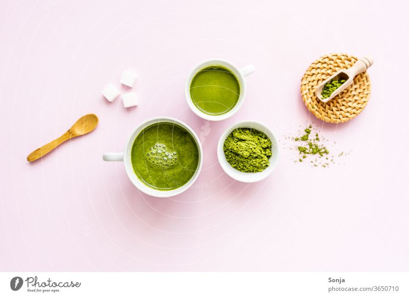 Matcha Latte in zwei weißen Tassen und Pulver in einer Schüssel auf einem rosa Hintergrund. Flat lay, Zutaten. grün Tee Getränk Matcha-Tee trinken Rührbesen