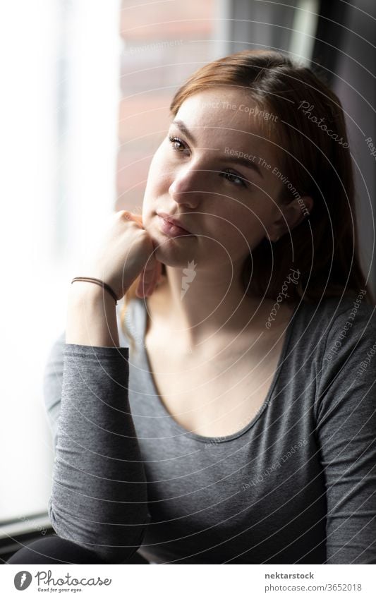 Schönes Porträt einer jungen Frau am Fenster sitzend mit der Hand auf dem Kinn eine Person Mädchen Junge Frau Hand am Kinn posierend im Innenbereich Pose