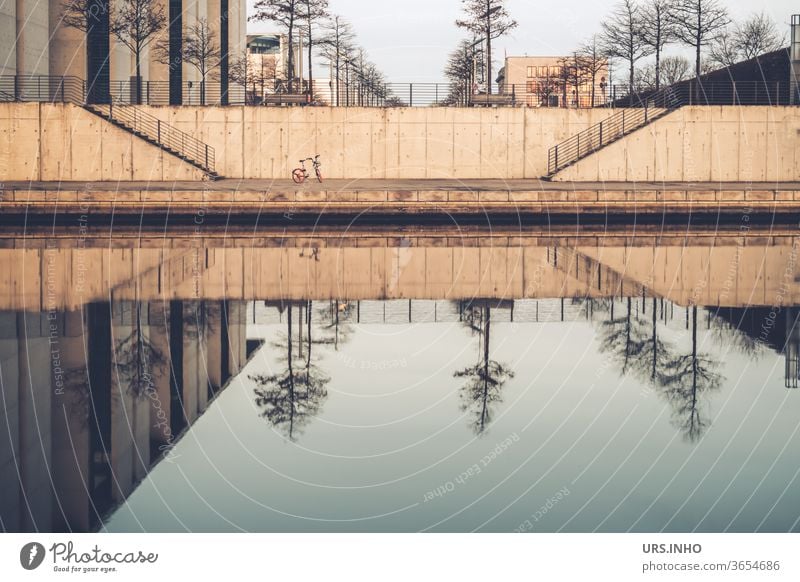 ein kleines Fahrrad steht einsam zwischen den Treppen am Spreebogen und betrachtet die Spiegelung der kahlen Bäume im Wasser Reflexion Ludwig-Erhard-Ufer Berlin