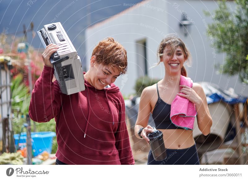 Aufgeregte Sportlerinnen mit Ghettoblaster im Hinterhof ruhen Boombox Land Glück aufgeregt zuhören Fitness Sportbekleidung sich[Akk] entspannen Training