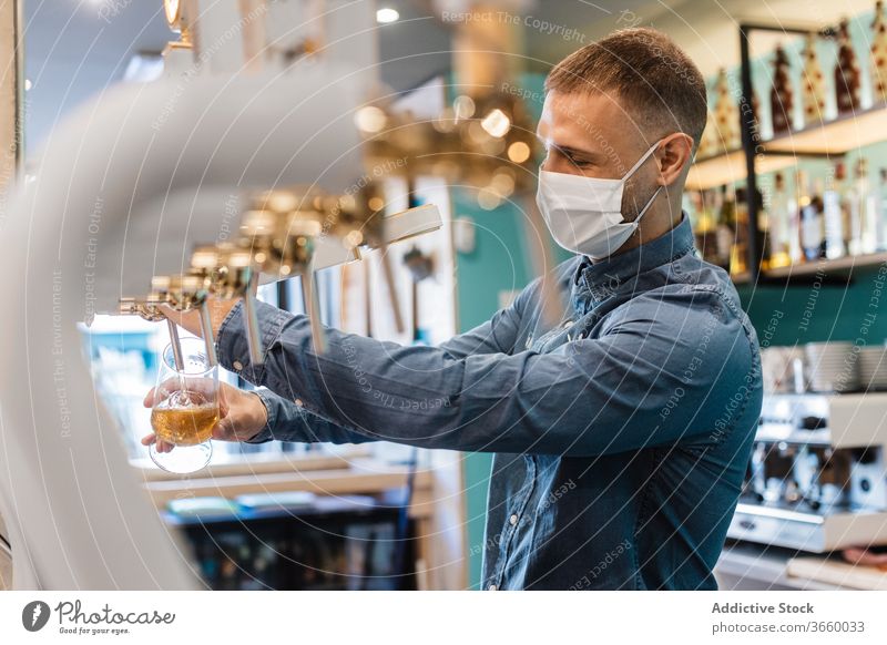 Junger Mann füllt Glas mit Bier für Kunde eingießen Wasserhahn frisch Barkeeper Mundschutz Pub Tiefgang Alkohol trinken Arbeit männlich jung Hemd positiv