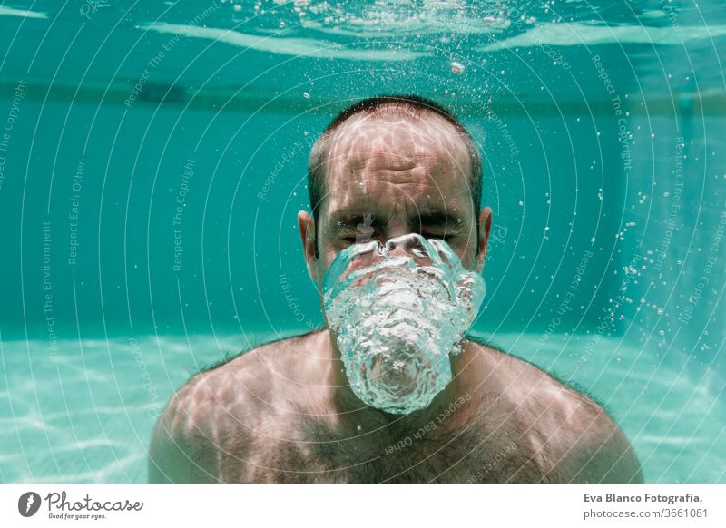 junger Mann taucht unter Wasser in einem Pool und macht Seifenblasen, Sommer und Spaß Schwimmsport Blasen Kaukasier Sinkflug Lifestyle übersichtlich Gesundheit