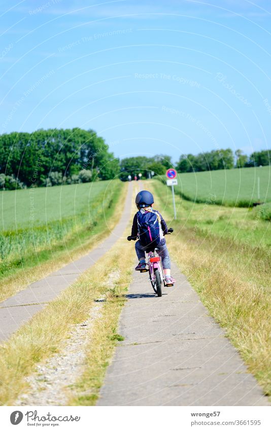 Nordwärts | Kind radelt auf einem Plattenweg Richtung Steilküste Mädchen radeln Ackerweg Feldweg Außenaufnahme Farbfoto Sommer Wege & Pfade Tag Kindheit Himmel