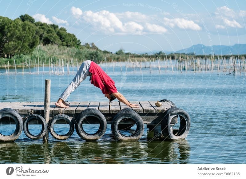 Fiter Mann verbessert Gleichgewicht während er die Natarajasana-Yoga-Pose am Meeresufer macht Herr des Tanzes gyan Mudra Dehnung Pier MEER friedlich üben Asana