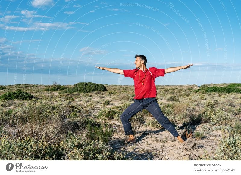 Männlicher Turner, der während des Yogatrainings in der Natur Beine und Arme streckt Mann Dehnung Asana Sand Gelände Gleichgewicht üben Übung