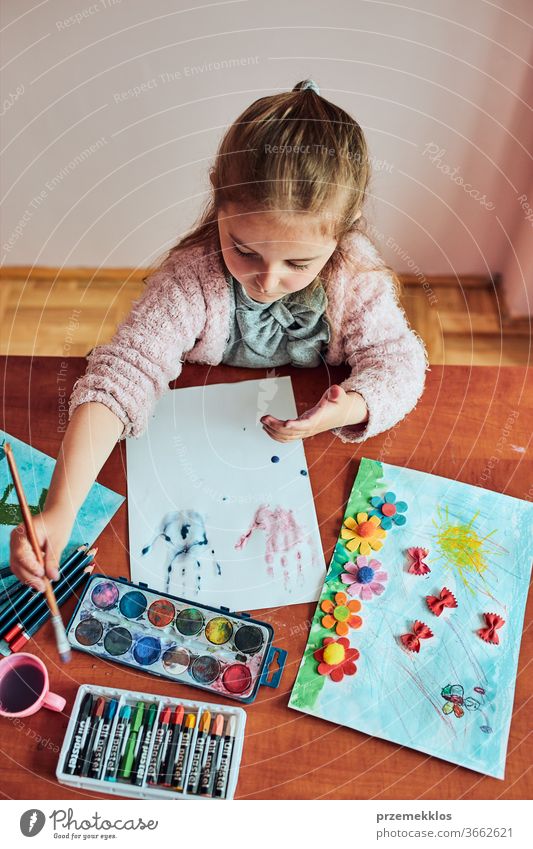 Kleines Mädchen im Vorschulalter, das mit bunten Farben und Buntstiften ein Bild malt. Kind, das während eines Kunstunterrichts im Klassenzimmer Spaß beim Malen eines Bildes hat