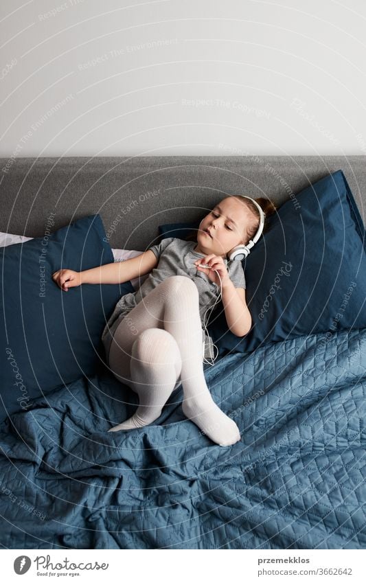 Kleines Mädchen singt mit Kopfhörerkabel in der Hand und imitiert sich selbst als echte Sängerin. Kind, das Spaß daran hat, beim Tanzen zu springen und Musik auf dem Bett im Schlafzimmer zu Hause zu hören