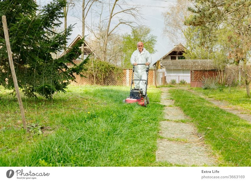 Landwirt in Schutzkleidung mäht Rasen in einem Garten mit einem Benzinrasenmäher Hinterhof Blütezeit botanisch Pflege Schermaschine kultivieren geschnitten