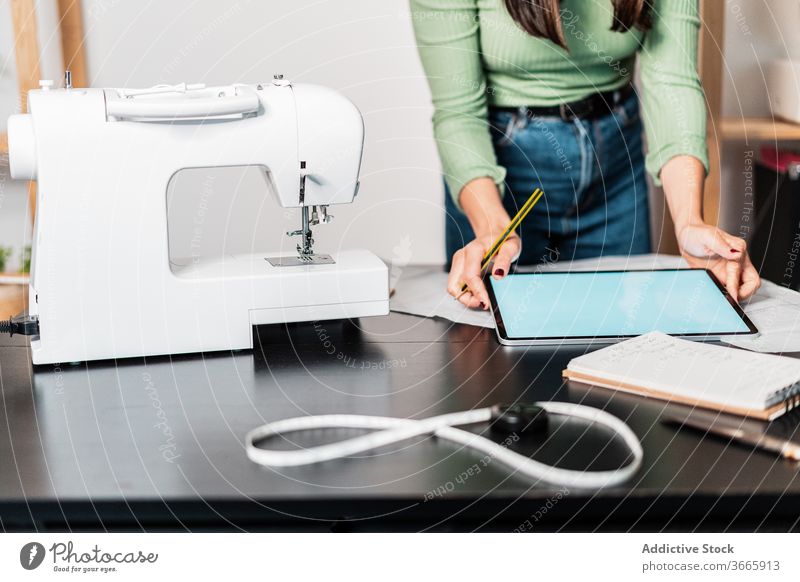 Schnittschneider mit Tabletten in der Nähe von Papieren und Nähmaschine Näherin messen Lineal Handwerk nach vorne lehnen Kleinunternehmen Arbeit Backsteinwand