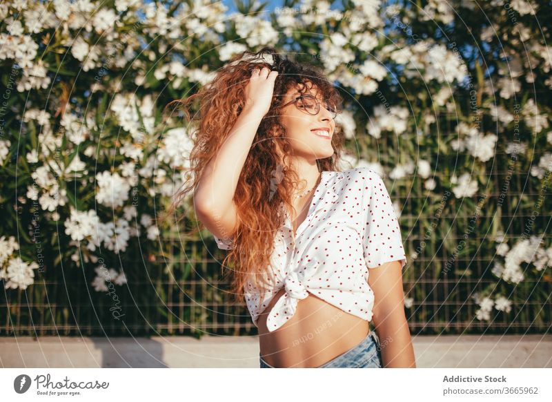 Positiv weiblich mit gewelltem Haar in der Nähe blühender Blumen stehend Frau Haare berühren Blütezeit Zaun gewelltes Haar Glück Schönheit Lifestyle Bauch