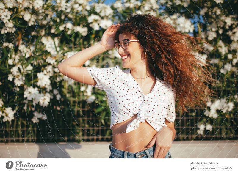 Positiv weiblich mit gewelltem Haar in der Nähe blühender Blumen stehend Frau Haare berühren Blütezeit Zaun gewelltes Haar Glück Schönheit Lifestyle Bauch