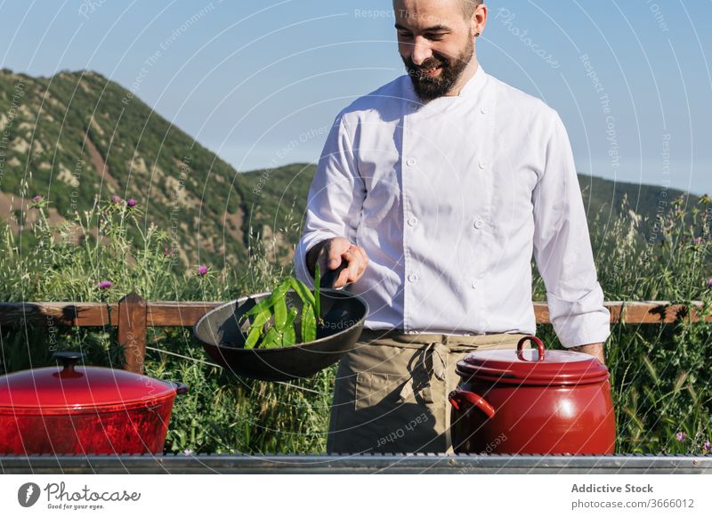 Profikoch kocht an einem sonnigen Tag auf dem Land Mann Koch Speise Gewürz Pfanne Natur Landschaft Küchenchef Werkstatt vorbereiten Glück professionell Vollbart