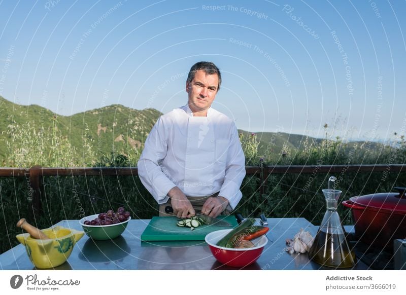 Männlicher Koch schneidet Gemüse für die Zubereitung des Abendessens in der Außenküche Mann geschnitten Salatgurke Küchenchef vorbereiten Speise frisch