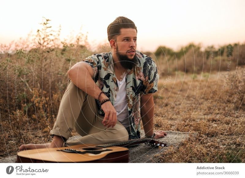 Fröhlicher Barfussgitarrist mit Gitarre im Feld Musiker Barfuß heiter Hipster Vorleger Gras Himmel Harmonie Mann Musical Instrument Gitarrenspieler spielen