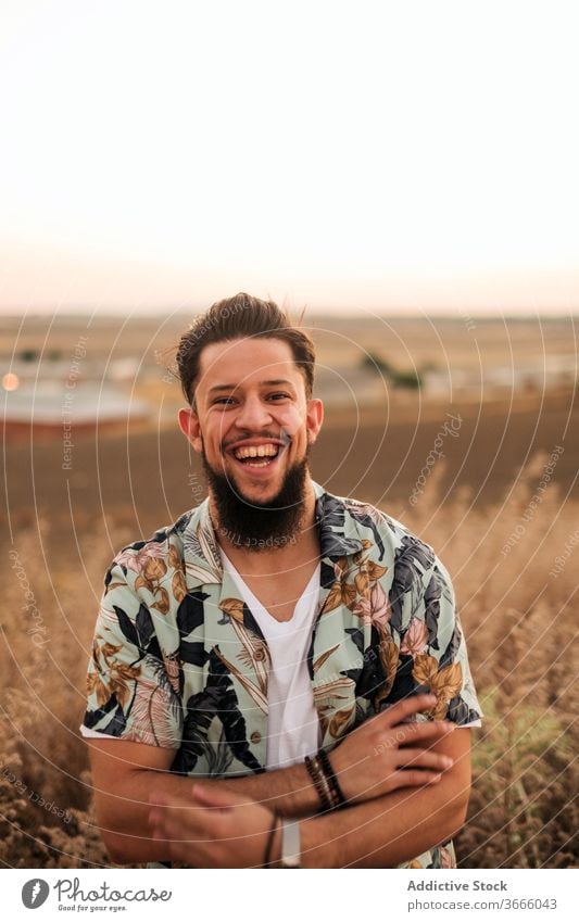 Glücklicher Hipster-Mann lacht im Feld bei farbenfrohem Sonnenuntergang Lachen genießen schlank Gras Landschaft Lifestyle positiv Vergnügen Abend selbstbewusst