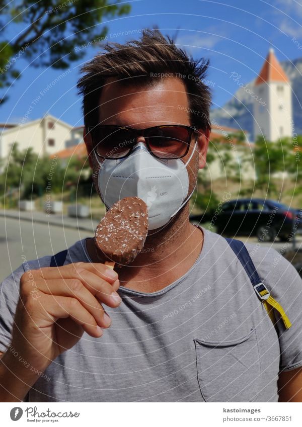 Junger Kerl in den Sommerferien, der eine Gesichtsmaske mit Coronavirus-Schutz trägt und nicht in der Lage ist, Eiscreme-Riegel zu lecken. Eiscreme-Bar