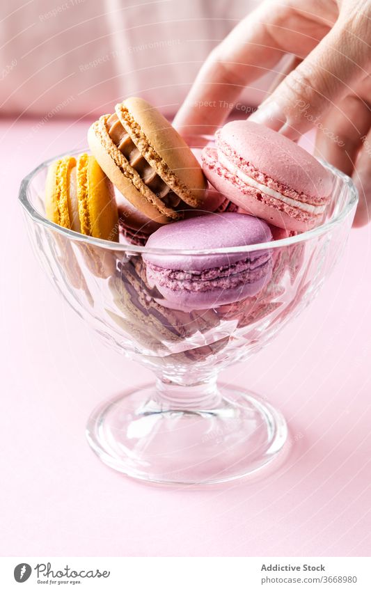 Frau nimmt köstliche Makronen aus Schüssel Macaron geschmackvoll lecker farbenfroh schmackhaft Gebäck Lebensmittel Küche Tisch Glas frisch Schalen & Schüsseln