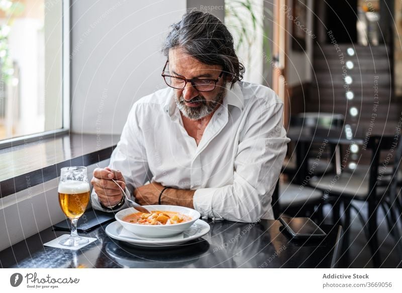 Bärtiger ethnischer Mann isst köstliches Mittagessen im Restaurant älter Café Glas Bier reif trinken positiv männlich ruhen Lächeln gealtert