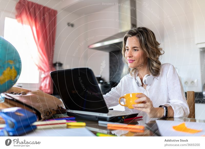 Positive Frau in Headset mit Videoanruf auf Laptop drinnen Tasse Heißgetränk Freizeit sprechen Lächeln benutzend Apparatur Gerät Netbook Gespräch Video-Chat