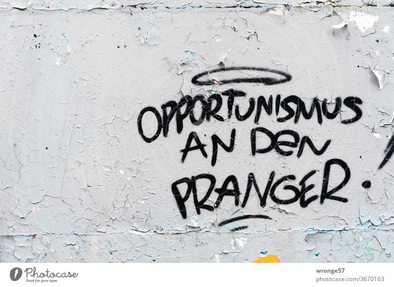 Opportunismus an den Pranger steht mit schwarzer Farbe an eine grauen Wand schwarze Farbe graue Wand alt abblätternd sprayen sprühen Graffitto Graffiti Mauer