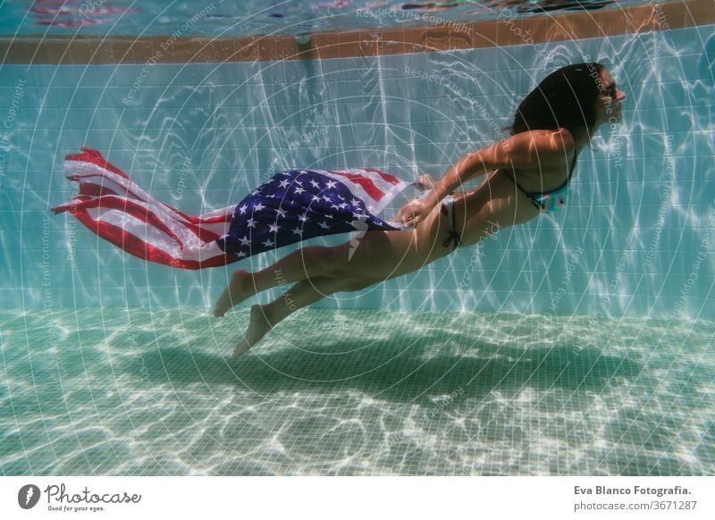 junge Frau in einem Pool, die die amerikanische Flagge unter Wasser hält. Konzept für den Unabhängigkeitstag am 4. Juli. Sommerzeit Stars and Stripes