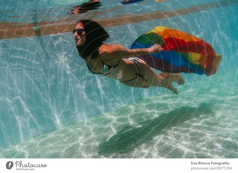 junge Frau in einem Pool, die unter Wasser eine Regenbogenflagge mit schwuler Flagge hält.LGBTQ-Konzept. Sommerzeit Schwimmbad Schwulenflagge lgbtq Beteiligung