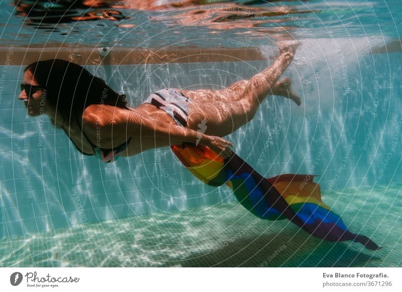 junge Frau in einem Pool, die unter Wasser eine Regenbogenflagge mit schwuler Flagge hält.LGBTQ-Konzept. Sommerzeit Schwimmbad Schwulenflagge lgbtq Beteiligung