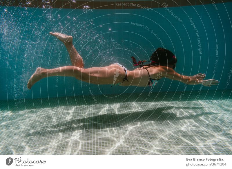 junge Frau, die in einem Schwimmbad unter Wasser taucht. Sommer und lustiger Lebensstil Sonnenbrille Schwimmsport Blasen Spaß Kaukasier Pool Sinkflug Lifestyle