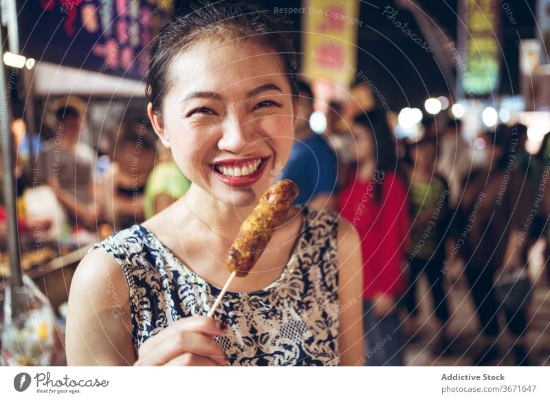 Ethnische Frau bläst auf gebratene Wurst auf der Straße Straßenessen Nacht Markt Lebensmittel Wurstwaren Schlag cool heiß Asiatische Küche asiatisch ethnisch