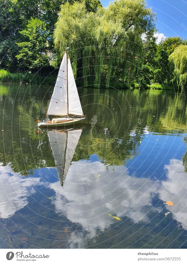 Ein Modellsegelboot segelt an einem Sommertag auf einem Weiher Segel Boot Segelboot Modellbau Wolken im Wasser Weiden Miniatur Segeln