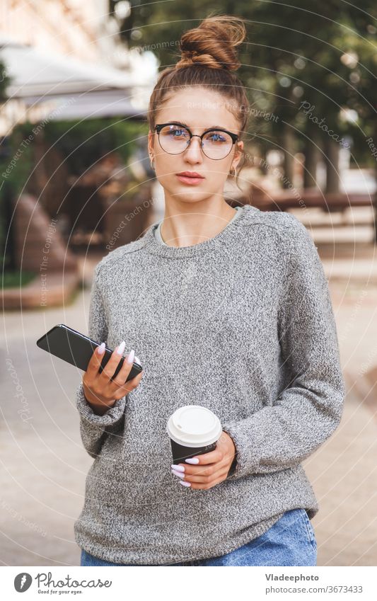 Junges Mädchen in Freizeitkleidung mit Smartphone und einer Tasse Kaffee zum Mitnehmen. Tägliches Leben der Jugend. Menschen online Frau jung Großstadt Internet