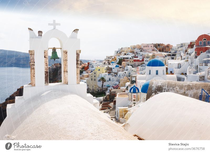 Blick auf das Meer und das Dorf Oia durch den traditionellen griechischen weißen Kirchenbogen mit Kreuz und Glocken im Dorf Oia auf der Kykladeninsel Santorin