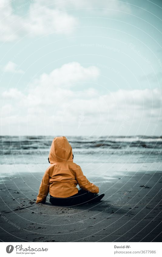 Kind mit Friesennerz am Strand beobachtet das Meer Kleinkind Junge Mädchen friesennerz niedlich beobachten Ozean Wellen dunkel düster alleine verlassen Gefahr